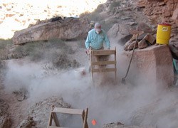 Screening for artifacts: Axehandle Alcove Lone archaeologist for artifacts at the dusty Axehandle Alcove site with wooden equipment.