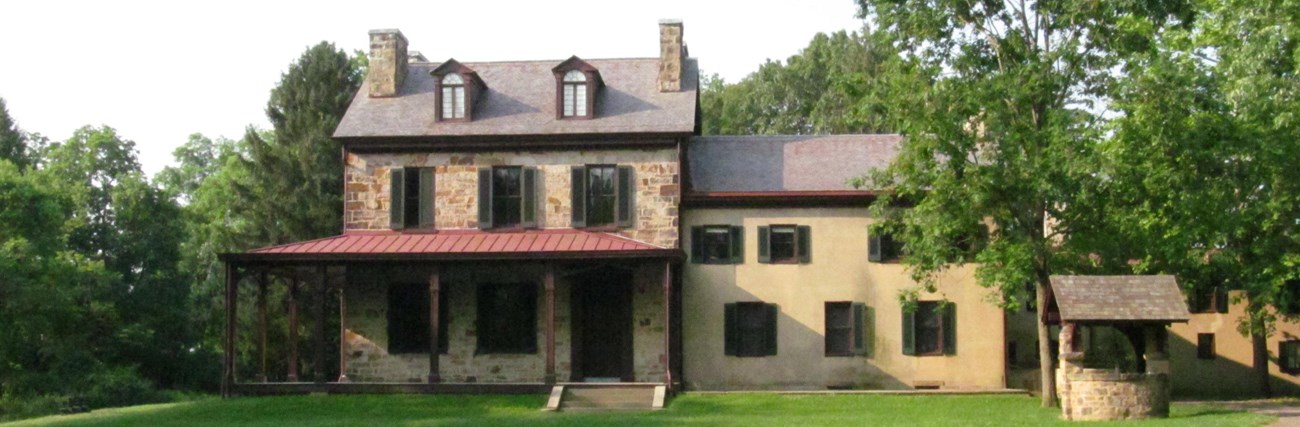 View of the front of the stone portion of the Gallatin House with green trees in the background. View of the front of the stone portion of the Gallatin House with green trees in the background.