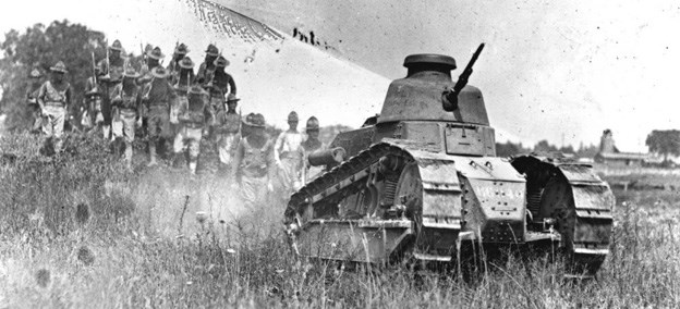 A Renault FT-17 tank rolls through the prairie, followed by infantry on foot.