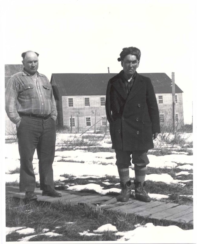 A historical photo of two men standing on a wood boardwalk in from of a cannery.