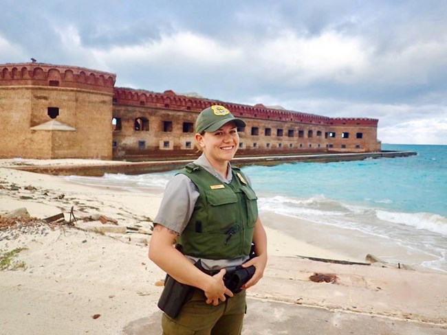 Woman in park ranger uniform stands in front of a stone fort.