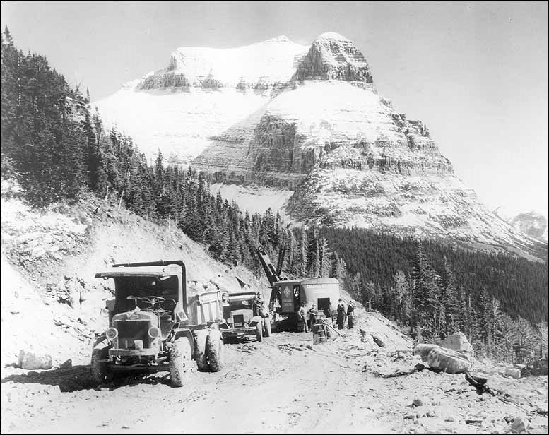 Trucks driving down a mountain road with large mountains int he background. National Park Service photo.