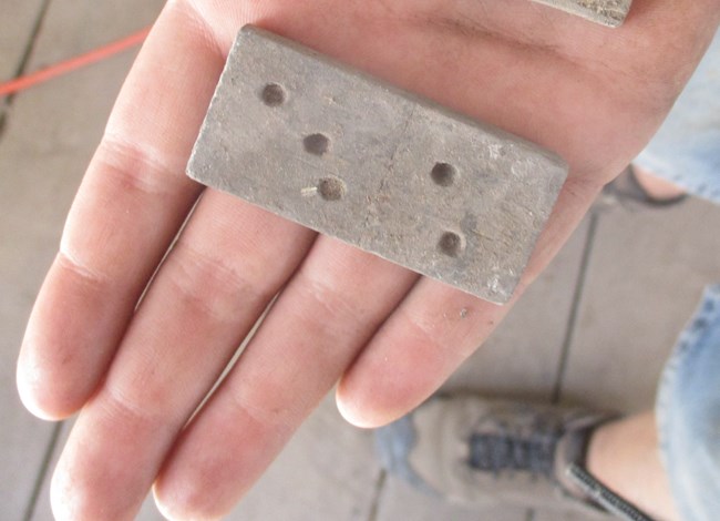 Hand holding a grey colored wood domino.