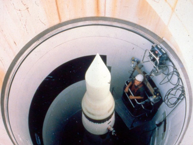 A young man is in a work cage suspended at the side of a deep missile silo