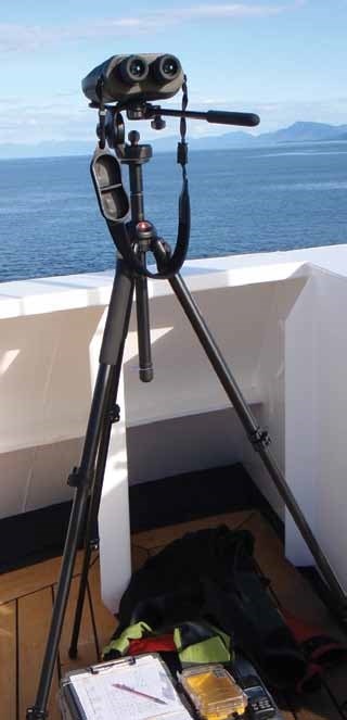 a pair of binoculars on a tripod set against the side of a boat with the ocean in the distance