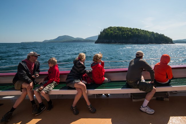 People sitting on a boat, looking out at open water and a small island.