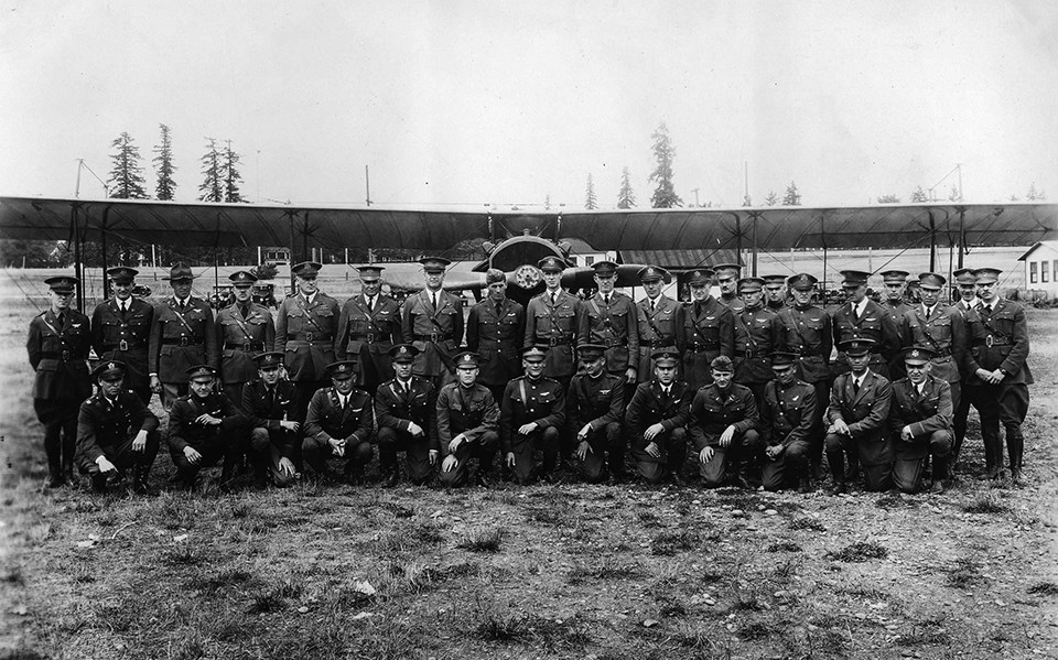 Black and white photo of men in military uniforms posing in front of a JN-4 Jenny aircraft.