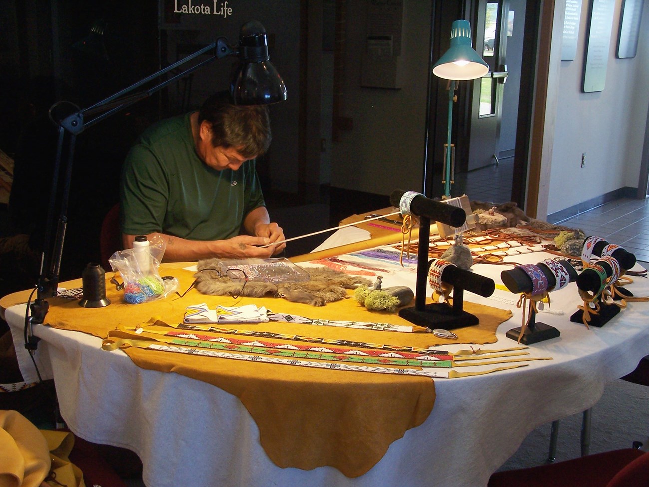 AGFO Visiting Artist Bob White Man working on a loom at a table covered in textiles