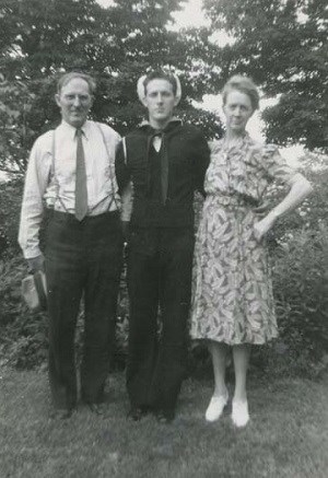 A man and women standing next to a young man in a navy uniform.