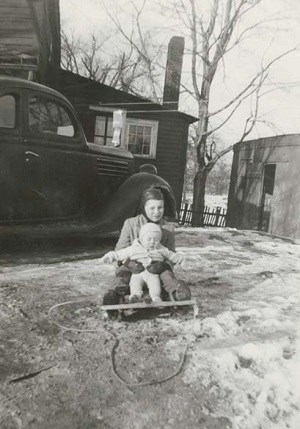 Kenneth and Ronnie Bass Two children on a sled in the snow with a car parked behind them.