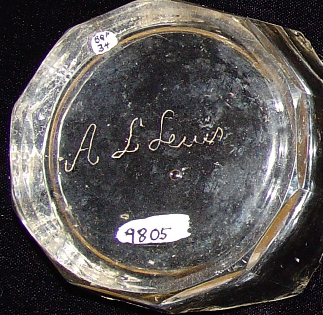 Photo showing the bottom of a glass tumbler. "A.L. Lewes" has been scratched into the glass.