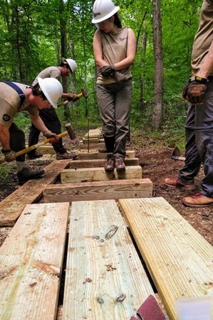Youths build a wooden trail in the woods.