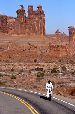 a cyclist wearing white rides in front of rock formations