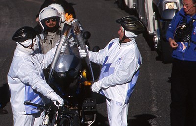 two people wearing white pass the Olympic flame from one torch to another