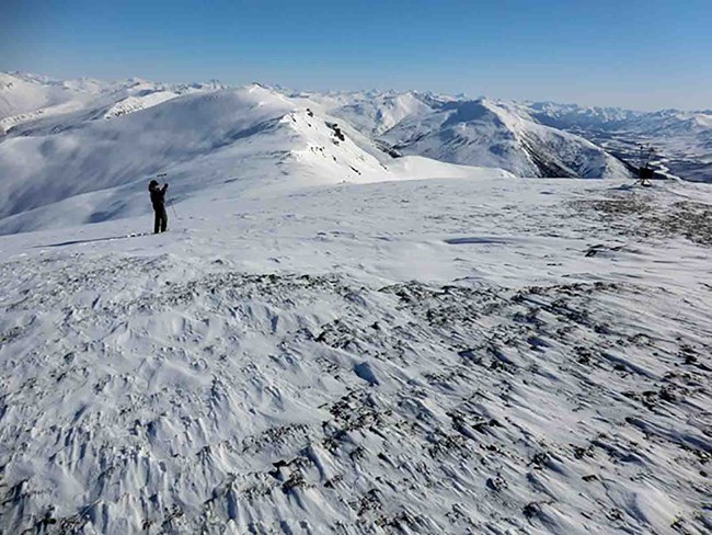 A researcher measures snow in the wind-swept Arctic Alaska mountains.