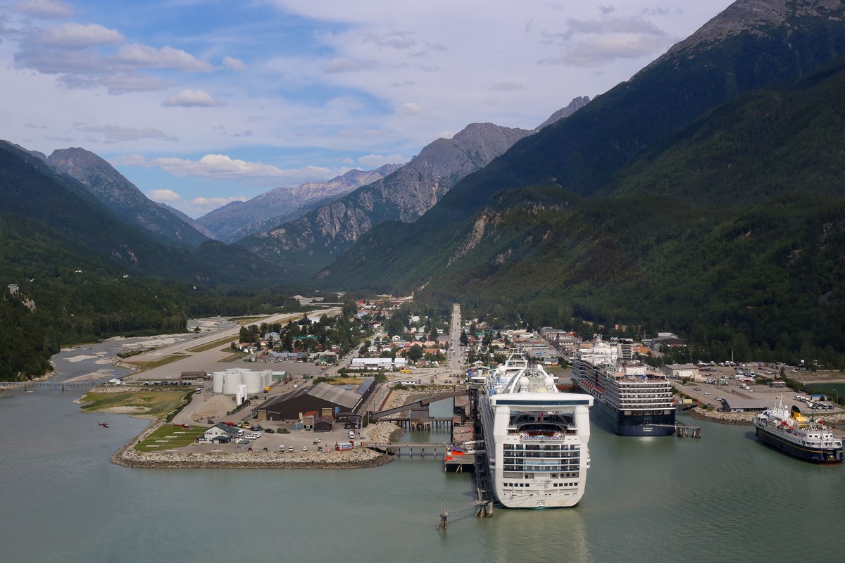 Cruise ships docked in town with mountain pass in background.