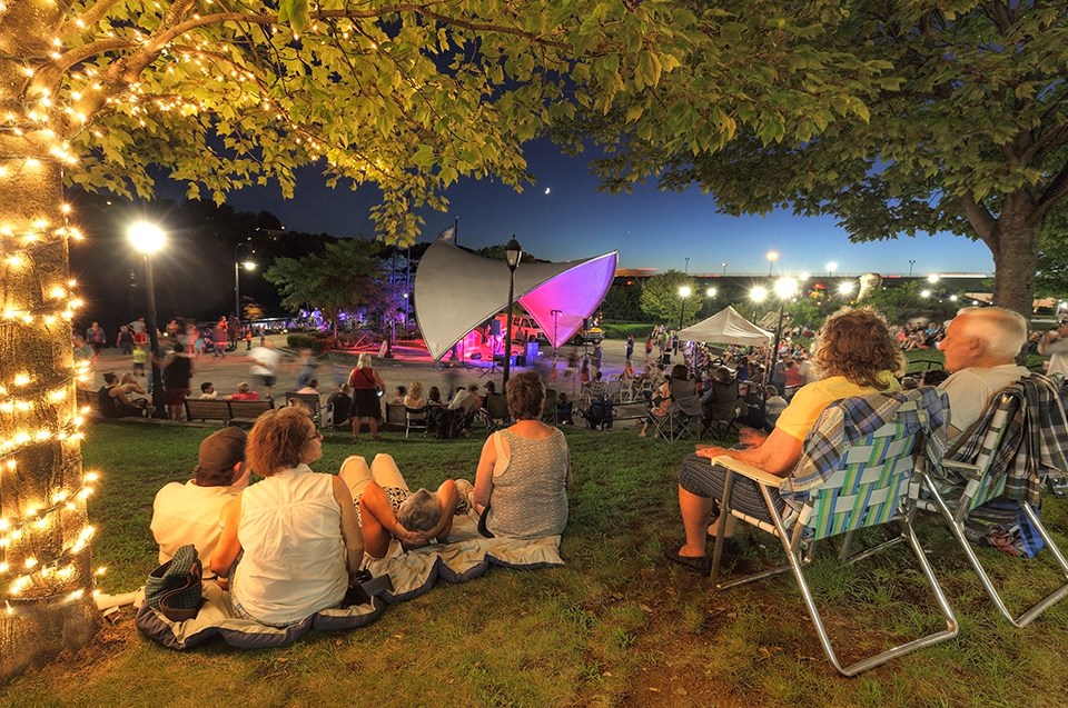 Men and women sitting on ground and chairs while watching a night concert.