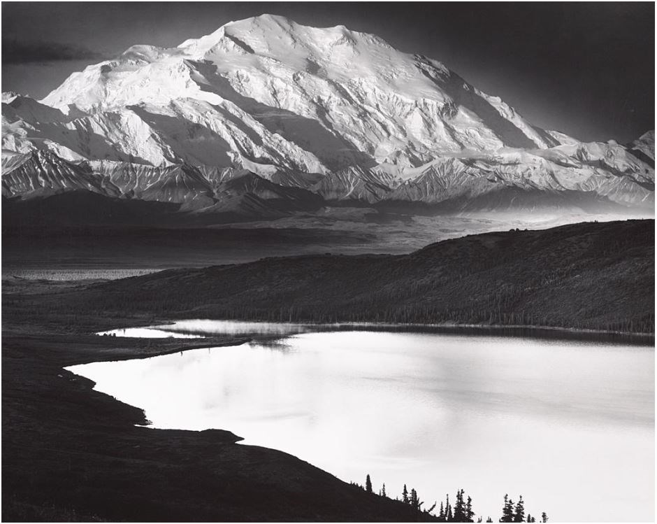 black and white photo of a huge snowy mountain overlooking a calm lake