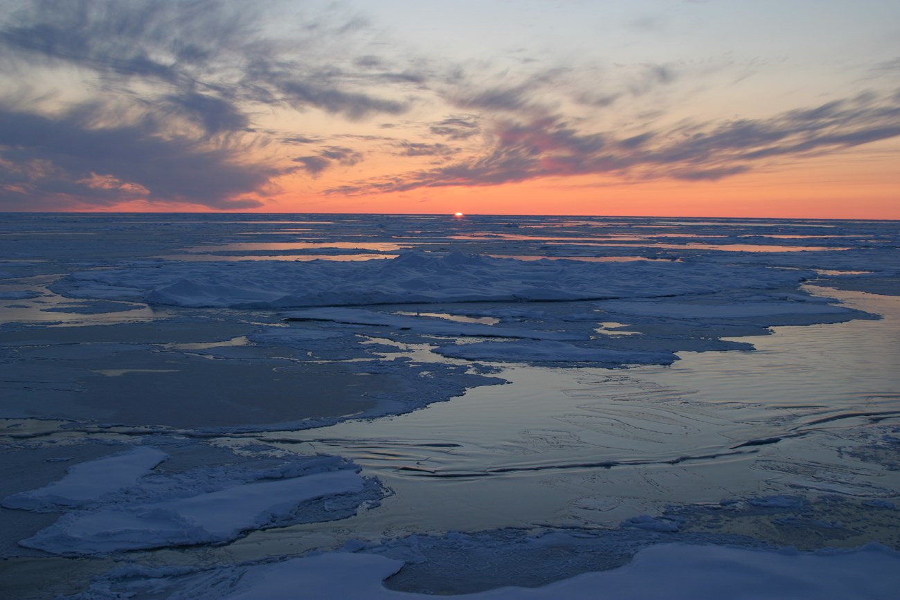 The setting sun casts an orange glow over the Arctic Ocean