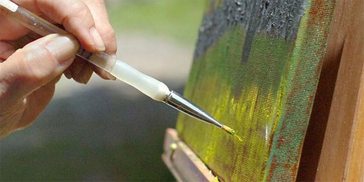 Close up image of a canvas with someone painting on it.