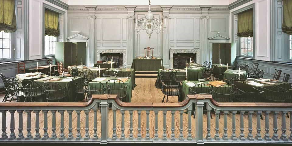 Color photo of a room with rows of tables covered with green cloth facing a central table.