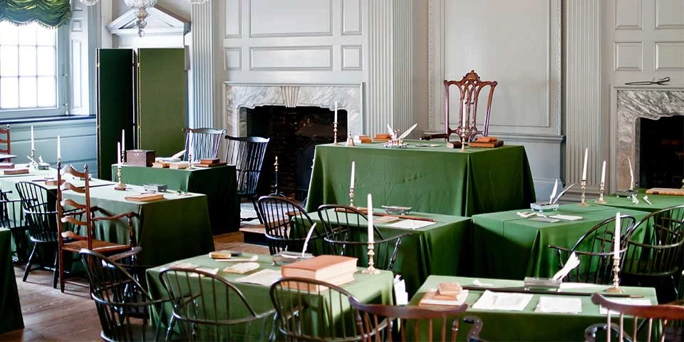 Color photo of a room with rows of tables covered with green cloth facing a central table. Color photo of a room with rows of tables covered with green cloth facing a central table.