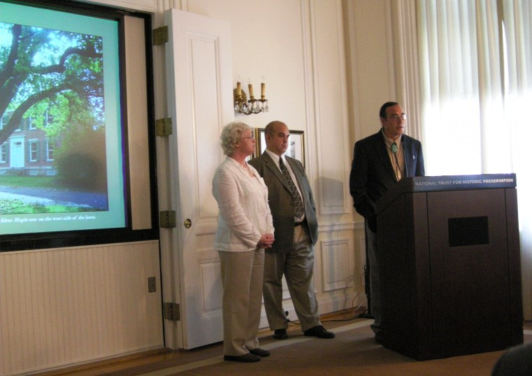 Three people standing in front of a screen with a podium in front.