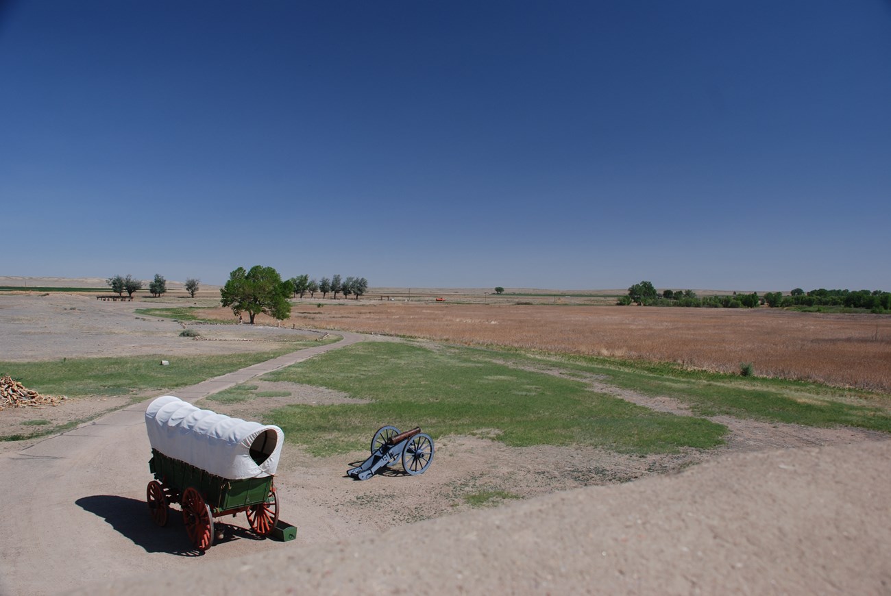 view of plains with covered wagon and cannon in foreground