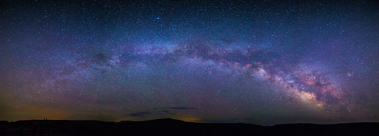 The Milky Way bends above a silhouetted landscape in this starfilled, panoramic view at Black Canyon of the Gunnison National Park, Colorado.