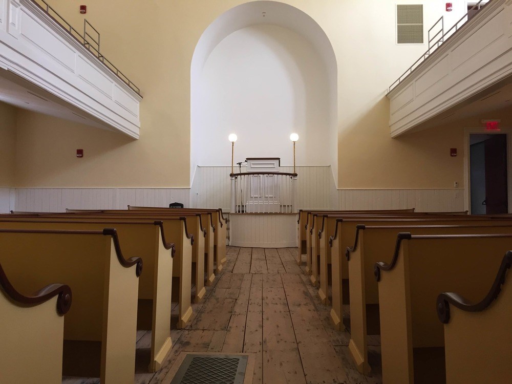 Interior of a church from behind rows of pews looking towards an altar.
