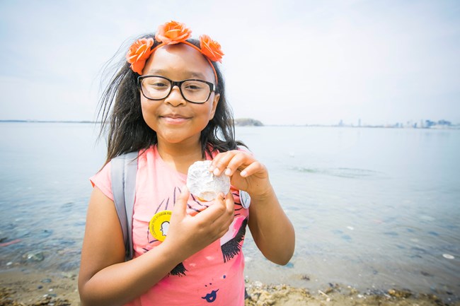 Kid holds up seashell she found on the beach.