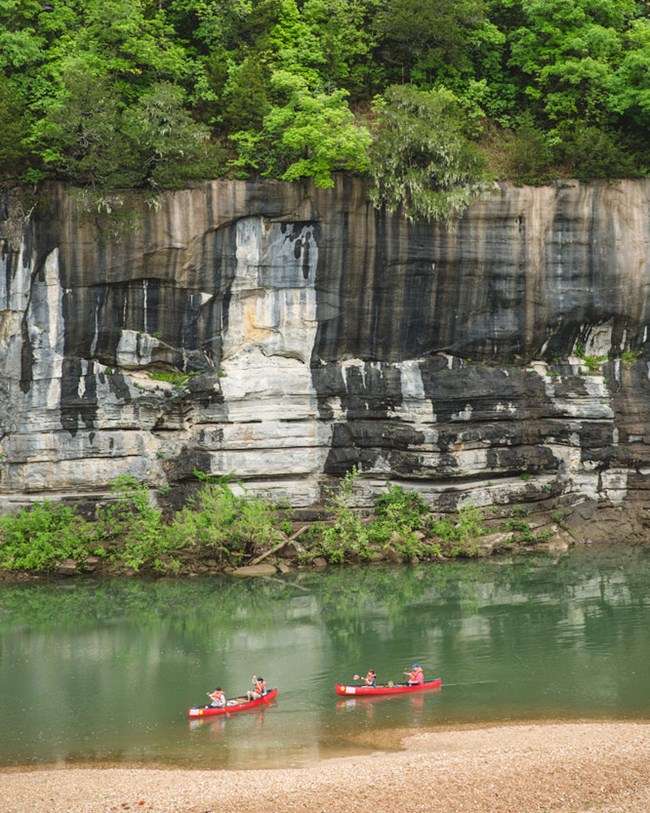 two canoes on river with rock bluff beyond
