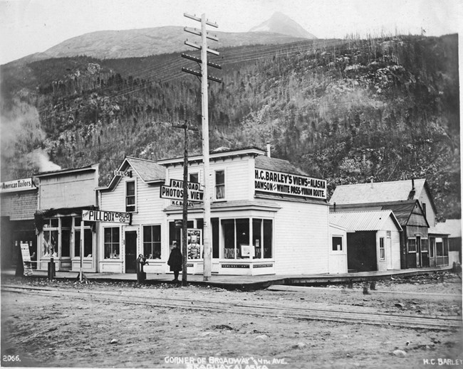 Black and white image of a corner store with sign "H.C. Barley's Views of Alaska"