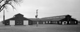 B&W image of a dark building with two white doors on the front and many windows.