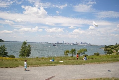 Children standing along sidewalk with water in the background, partly cloudy blue skies overhead.