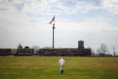 Boy holds a white kite. Across the field is Fort Stanwicx