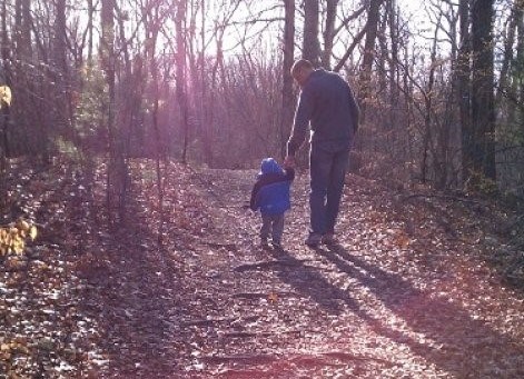 Man helps small child along a trail