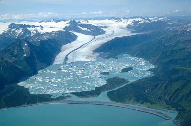 A large glacier descends from the mountains emptying into an iceberg-filled lagoon.