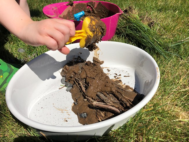 Photo of a mud, stone, and twig dam inside a baking dish.