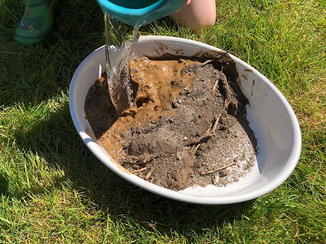 Photo of a child pouring water on one side of a dam built inside a baking dish.