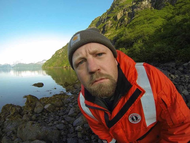 A close up of Ben looking at a GoPro on the beach.