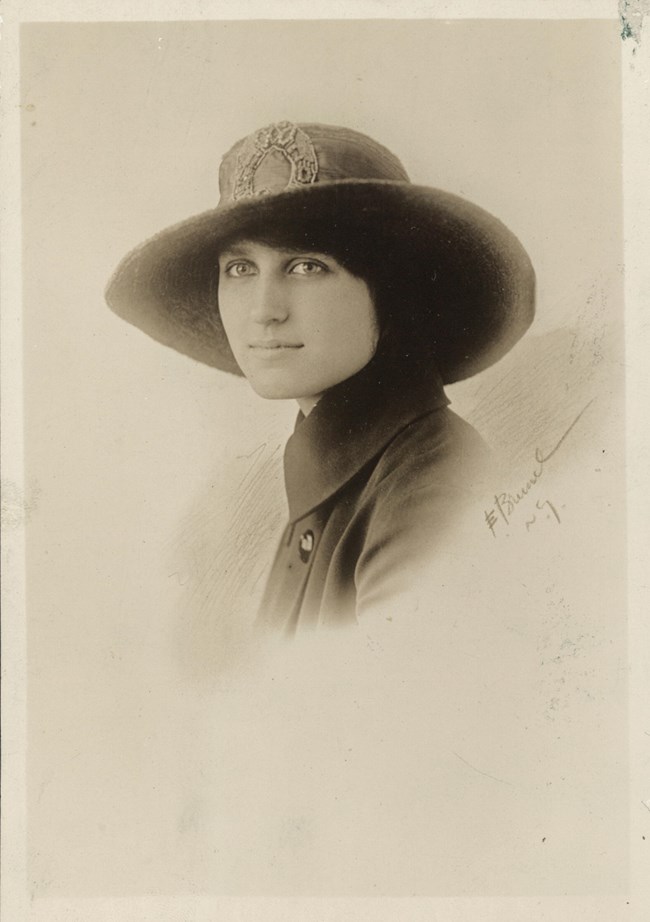 Formal portrait, head and shoulders, Beulah Amidon, facing left with head turned toward camera, wearing a broad-brimmed hat.