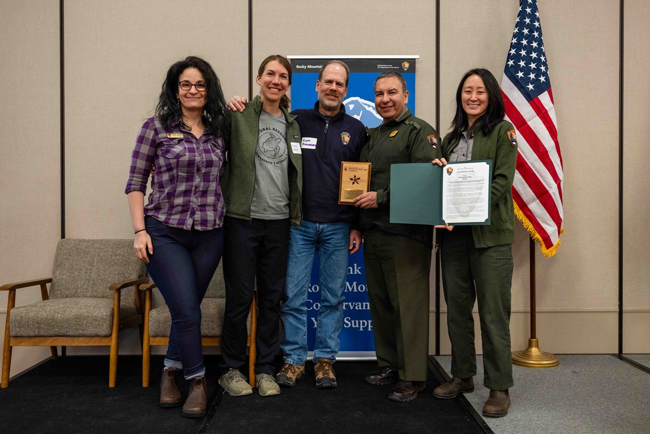 Three recipients stand on stage with two park staff to recieve an award