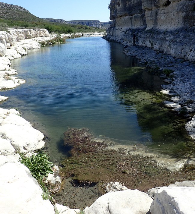 Big Satan Canyon Spring A large narrow pool of water surround by rock faces.
