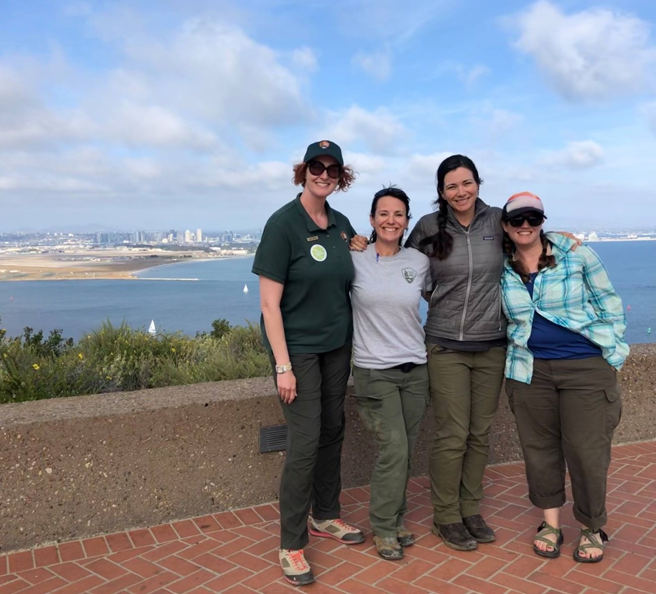 Four women pose for a picture in front of the backdrop of the city of San Diego. Two of the women are scientists from Cabrillo National Monument, and two of the women are scientists from Joshua Tree National Park.