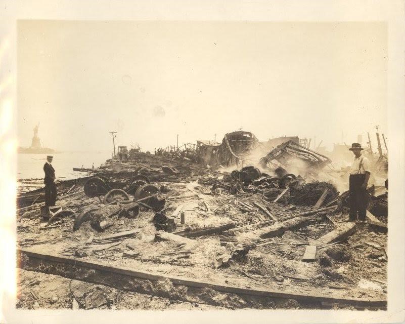 Pile of rubble with a man standing nearby and the Statue of Liberty in the distance