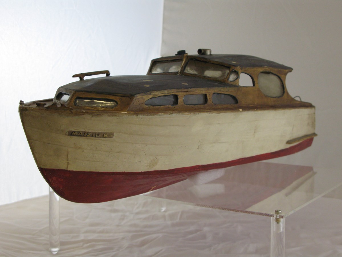 Image of a model boat painted red and white with "Maizie B." written on bow.