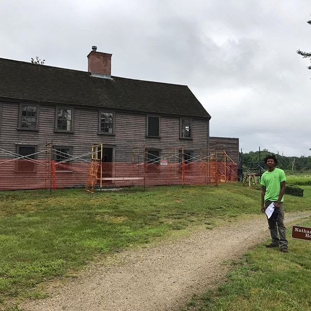 A young man poses in front of an historic structure being repaired.