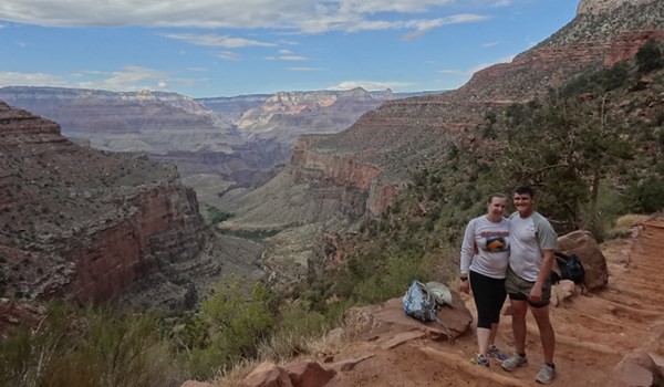 A man and woman stand at point overlooking the Grand Canyon.