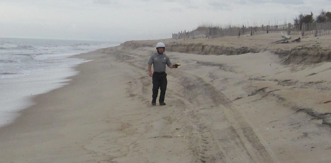 Konrad Losch (CAHA GIS Specialist) walking the high-tide line. Man standing on the beach in a hard hat and uniform